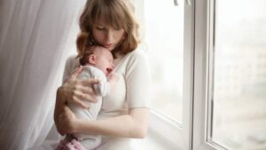Mamma håller ett gråtande spädbarn intill ett ljust fönster