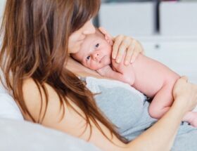 Mamma håller en nyfödd bebis nära kroppen i en lugn hemmamiljö