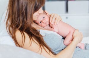 Mamma håller en nyfödd bebis nära kroppen i en lugn hemmamiljö