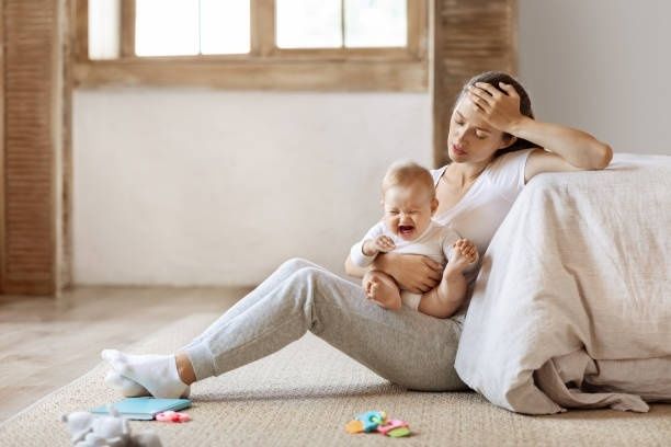 Trött mamma håller ett gråtande spädbarn på golvet