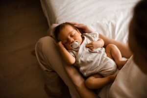 Sovande spädbarn med napp vilar tryggt i en vuxens famn